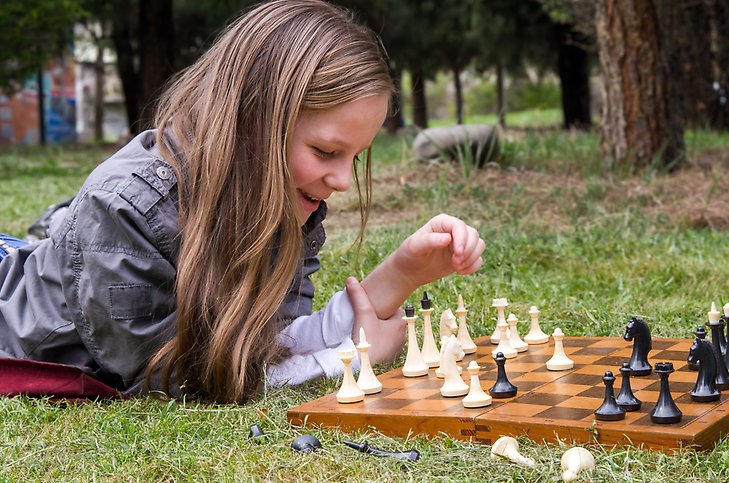 Flicka på fritidshem spelar schack ute i gräset