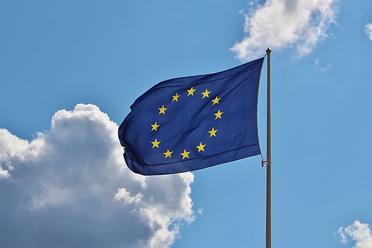 En blå EU-flagga mot blå himmel och några vita moln.