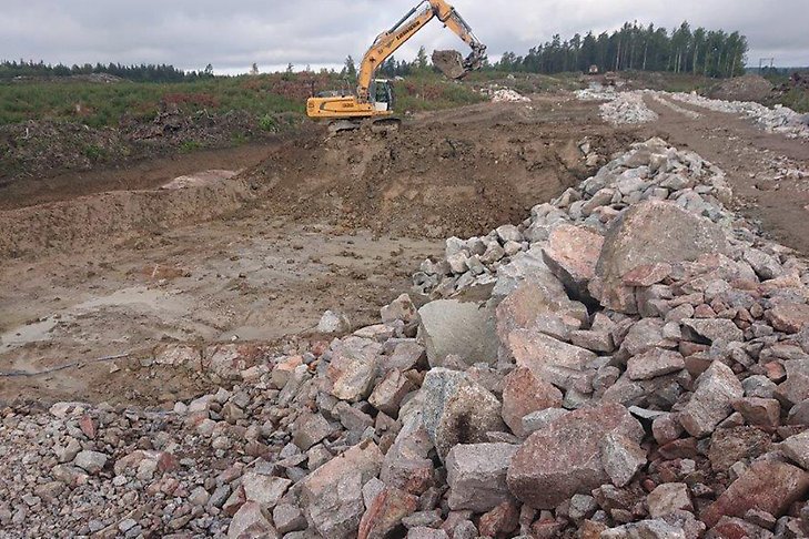 Stor stenhög och grävmaskiner som utför förarbeten med ny väg och skyddsvall