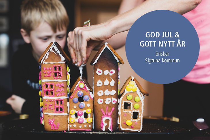 Två personer som bygger pepparkakshus med texten God jul och gott nytt år önskar Sigtuna kommun.