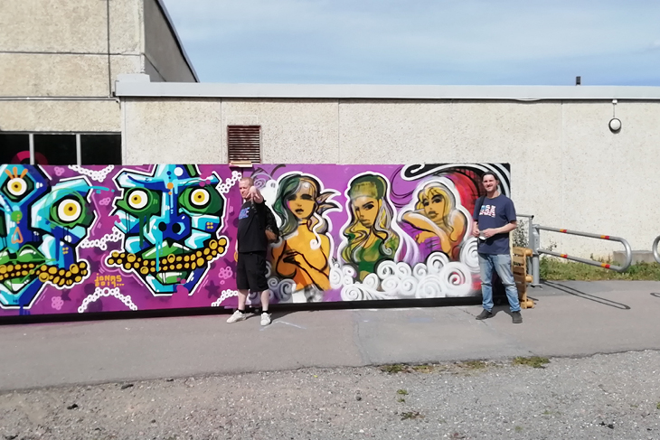 En tjej och en kille målar street art på en vägg utanför Valsta simhall. 