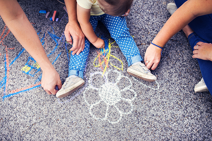 Ett barn och två vuxna målar blommor med asfaltskritor. Fotograf: Mostphotos
