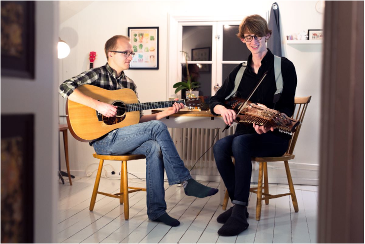 Två personer spelar musik tillsammans på gitarr och nyckelharpa. 