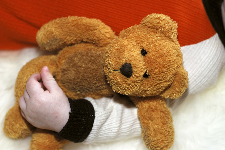 Ett barns arm håller fast en brun nallebjörn. 