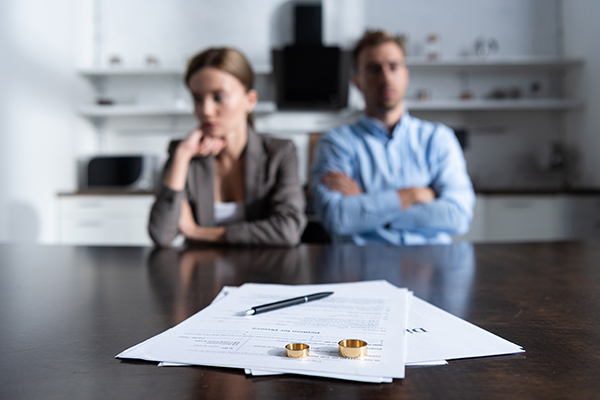 En kvinna och en man vid ett bord, med skilsmässopapper och vigselringar framför sig. 