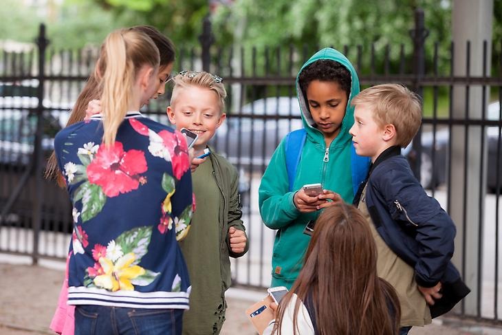 Några barn står i en cirkel med sina mobiltelefoner.