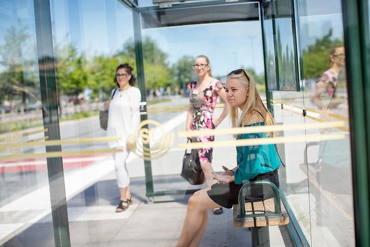 Tre personer väntar på bussen vid en busshållplats på Märsta station.