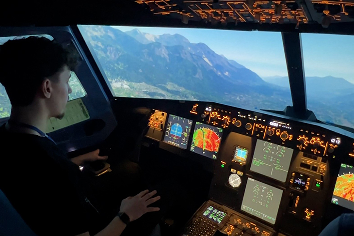 En tonårskille, elev på flygteknikutbildningen, sitter i en uppbyggd flygplanscockpit med reglage och knappar runt sig. Genom simulatorns rutor ser han ett alplandskap. Simulatorn imiterar en flygsituation. 