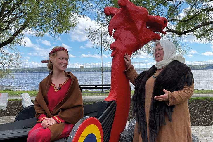 Två personer iklädda historisk klädsel sitter i en vikingabåt vid Mälaren.