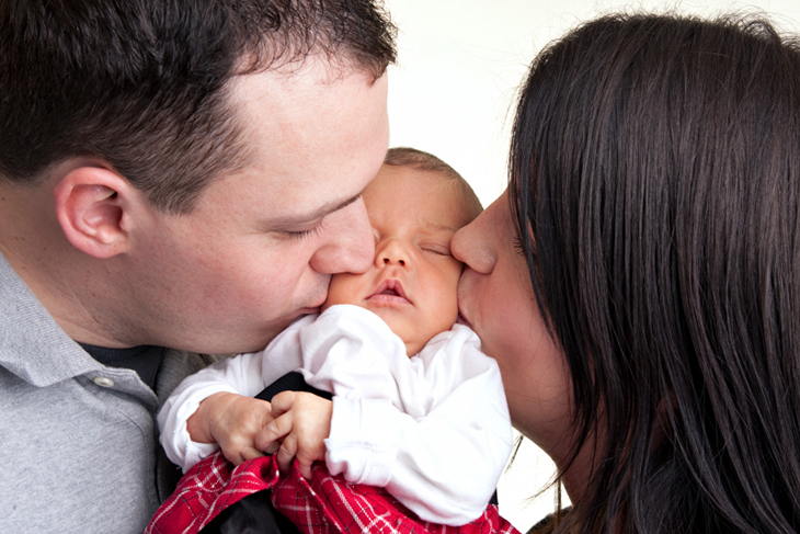 En mamma och en pappa pussar sin nyfödda bebis. 