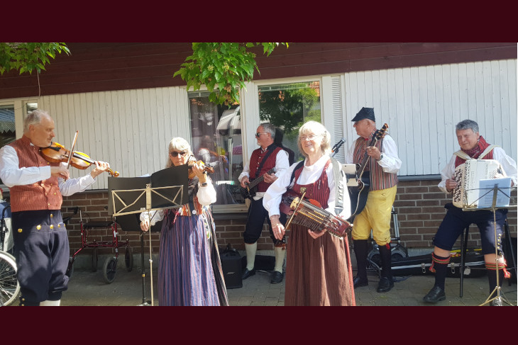 Flera personer spelar instrument klädda i traditionella folkdräkter från olika delar av Sverige. 