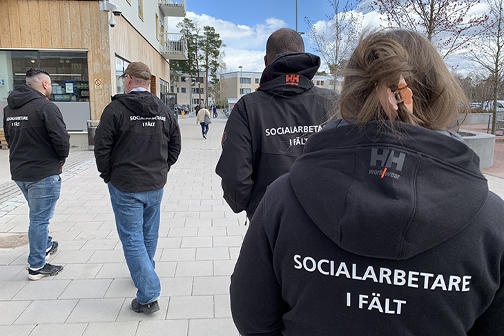 Fyra personer går i en stadsmiljö. De har svarta jackor på sig med texten socialsekreterare i fält på ryggen.