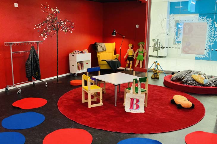 Ett färgglatt rum med röda väggar och röda och blåa mattor samt fåtölj och andra utrymmen för läsning.