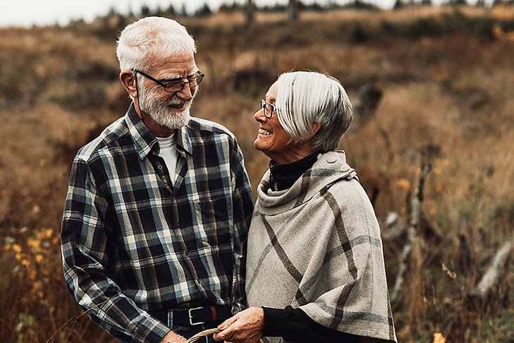 Äldre kvinna och man ser kärleksfullt på varandra, med en svampkorg i naturen.