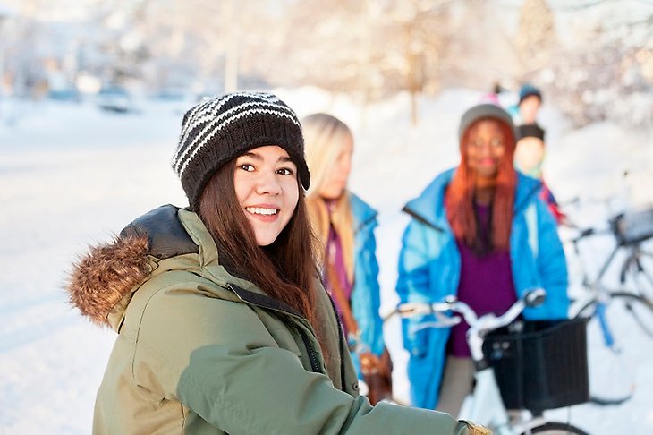 Tre unga tjejer står utomhus en vinterdag intill några cyklar 
