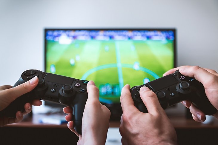 Två par händer håller i en varsin tv-spelskontroll framför en tv som visar spelet Fifa.