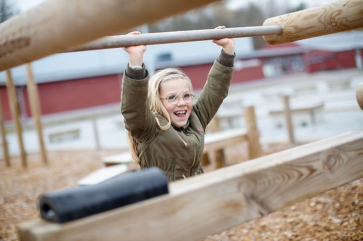 Ett barn ler stort när hon tränar i utegymmet i Rosersberg.