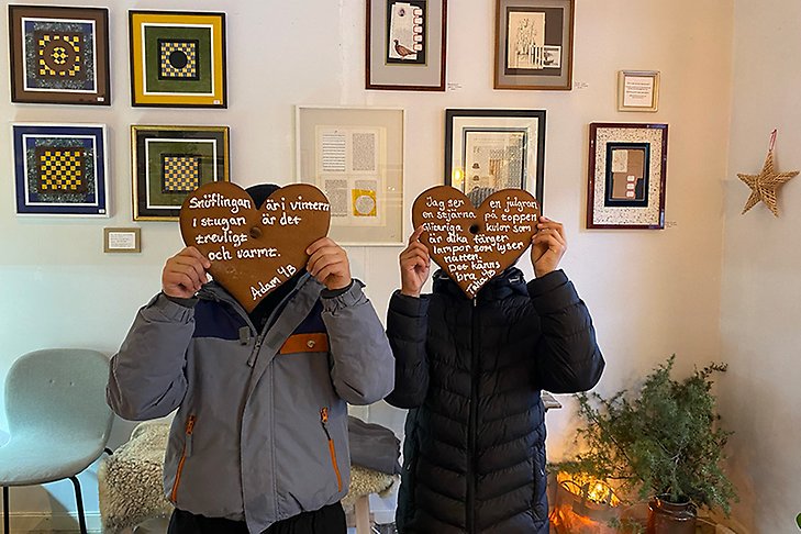 Två barn visar upp pepparkakor med dikter skrivna i kristyr. 