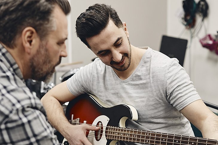 En ung kille blir instruerad av en gitarrlärare. 