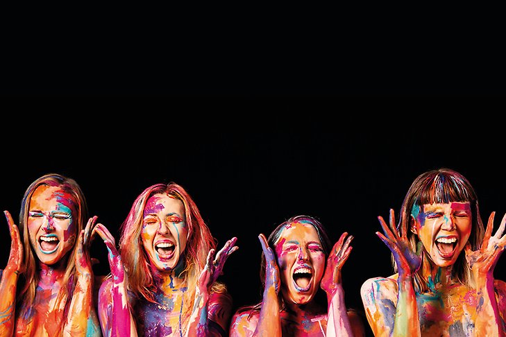 Fyra kvinnor är målade med färg och sjunger tillsammans. 