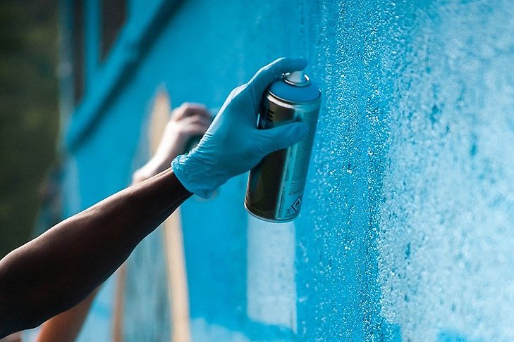 Två händer som målar på en graffitivägg med sprayburkar.