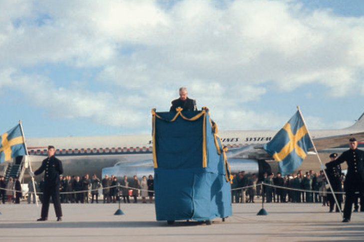 Kung Gustav VI Adolf i talarstolen, en blåskrudad flygplanstrappa, under invigningen av Arlanda 1962.