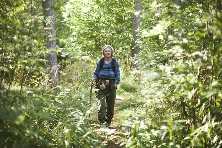 Äldre kvinna vandrar i tät skog.