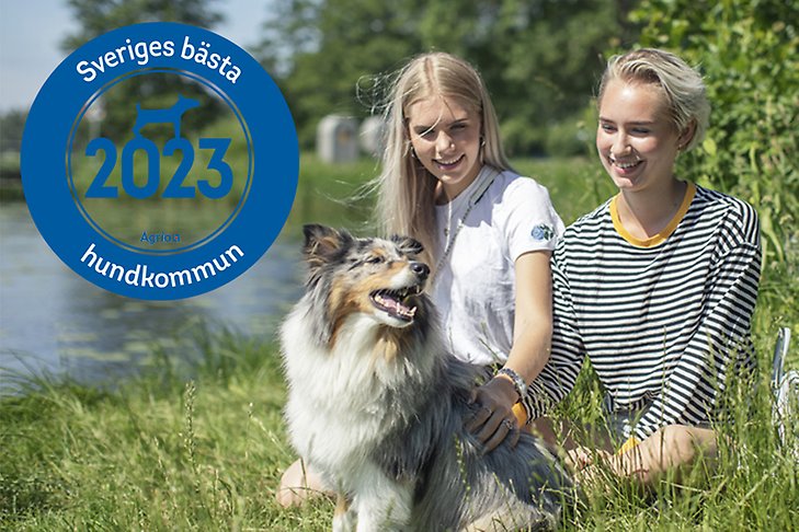 Emblem Sveriges bästa hundkommun 2023 på en bild av två unga tjejer som sitter i gräset med en hund intill ett vattenbryn. 