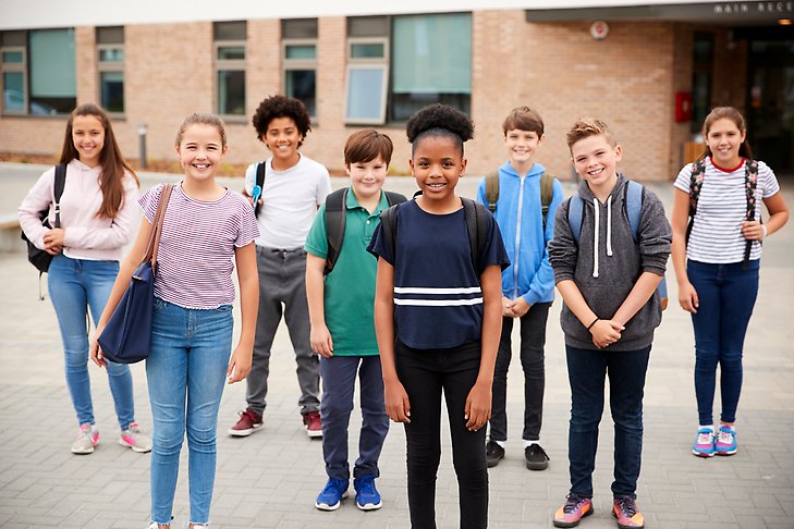 Grupp av elever står leende framför sin skola