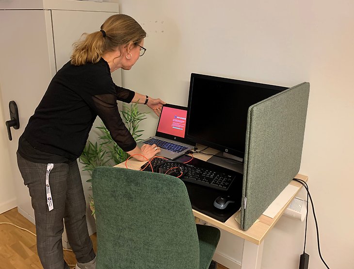 En kvinna öppnar och tittar på en dator vid en teststation med stor skärm. 