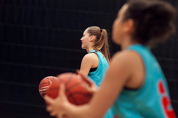 Två tjejer spelar basket inne i en hall. 