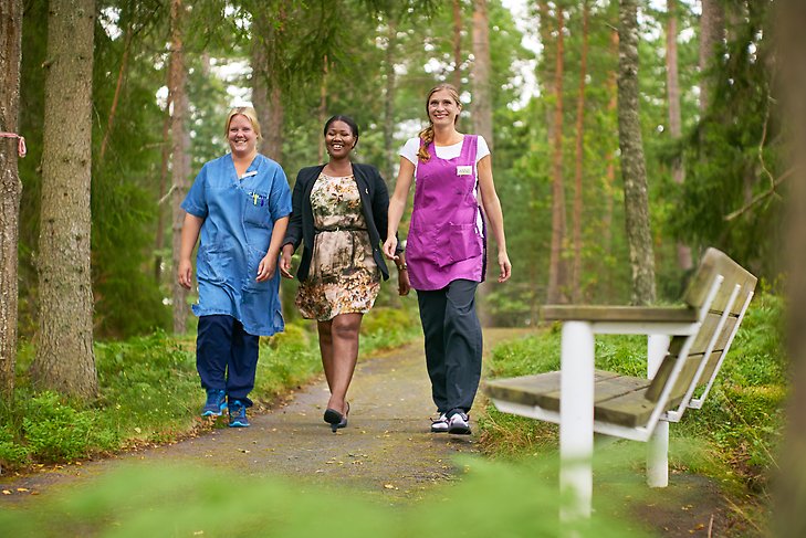 Tre kvinnor som jobbar med olika yrken inom vården går i en skog. Foto: Rosie Alm
