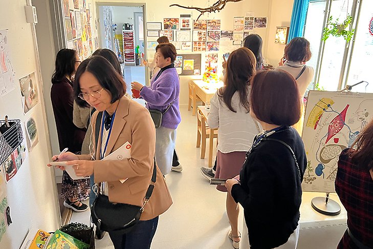 Flera asiatiska kvinnor står i ett förskolerum och tittar på det som finns på väggarna och gör anteckningar.