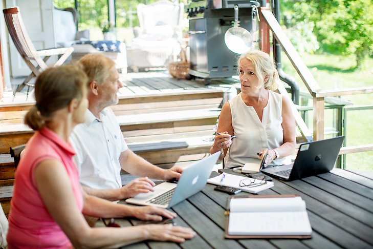 Två kvinnor och en man sitter och samtalar med varsin laptop vid ett bord utomhus.