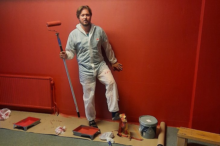 Marcus Modh målar väggarna röda och fastnar med foten i tejp.