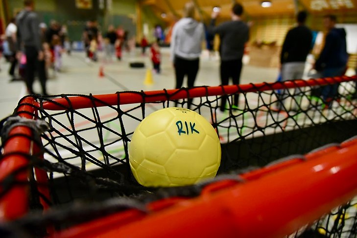 En gul boll som det står RIK på ligger ovanpå ett innebandymål i Råbergshallen
som är full med barn och vuxna. 
