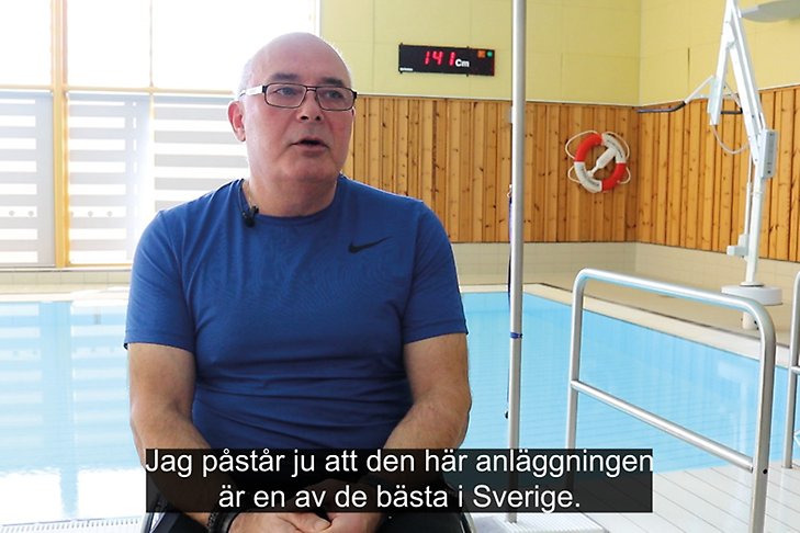 Tommy sitter i rullstol framför Midgårdsbadets rehabbassäng. Undertext "Jag påstår ju att den här anläggningen är en av de bätsa i Sverige."