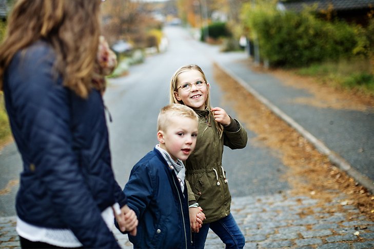 Två barn håller varandra i handen och går över en gata i Rosersberg tillsammans med en vuxen.