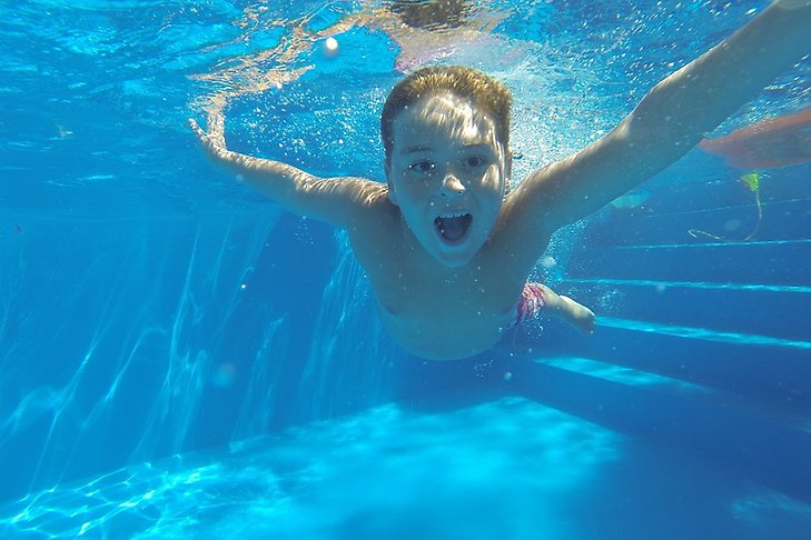 En pojke leker under vattenytan i en bassäng