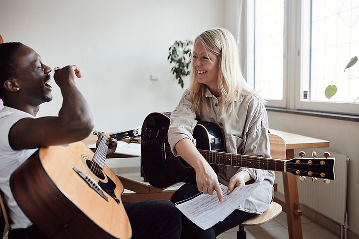 En kvinna lär ut gitarr till en ung elev som skrattar. 