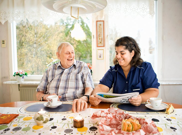 Äldre man och omsorgspersonal skrattar tillsammans. Foto: Susanne Kronholm/Johnér