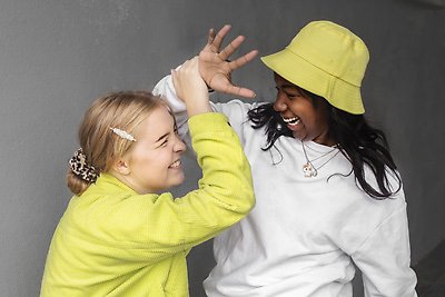 Två unga tjejer iklädda vita och gula kläder busar med varandra och skrattar. Foto: Johnér