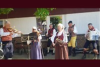 Flera personer spelar instrument klädda i traditionella folkdräkter från olika delar av Sverige. 