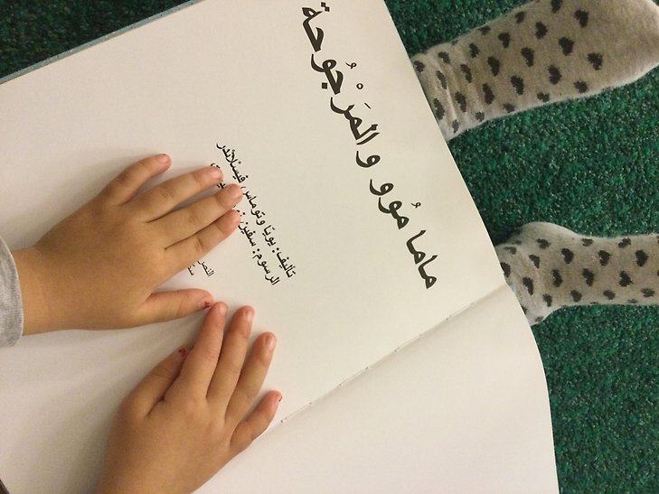 Barnhänder som följer läsningen ur en bok. Foto: Sigtuna kommun