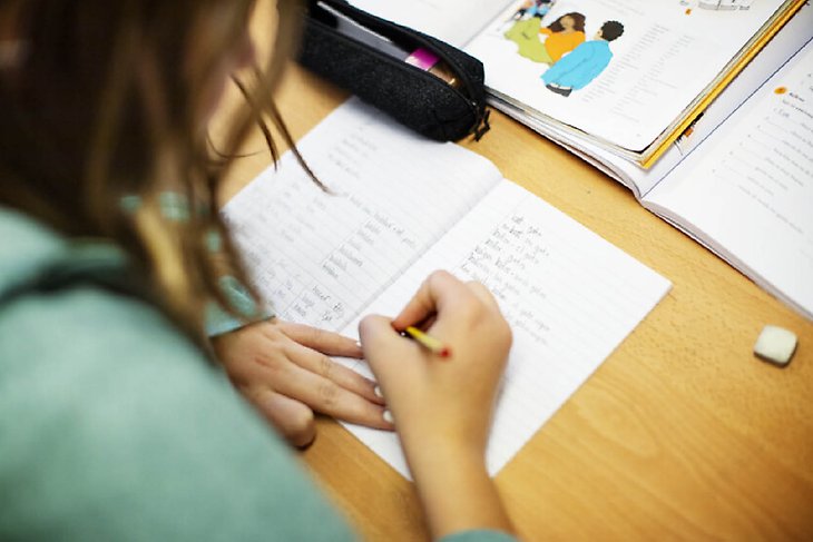En elev sitter ned vid skolbänken och antecknar i sitt anteckningsblock.