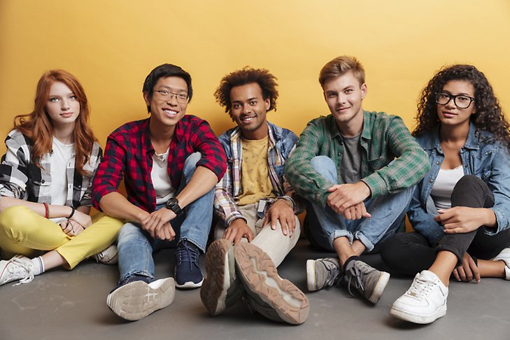 Fem glada ungdomar sittande framför gul vägg